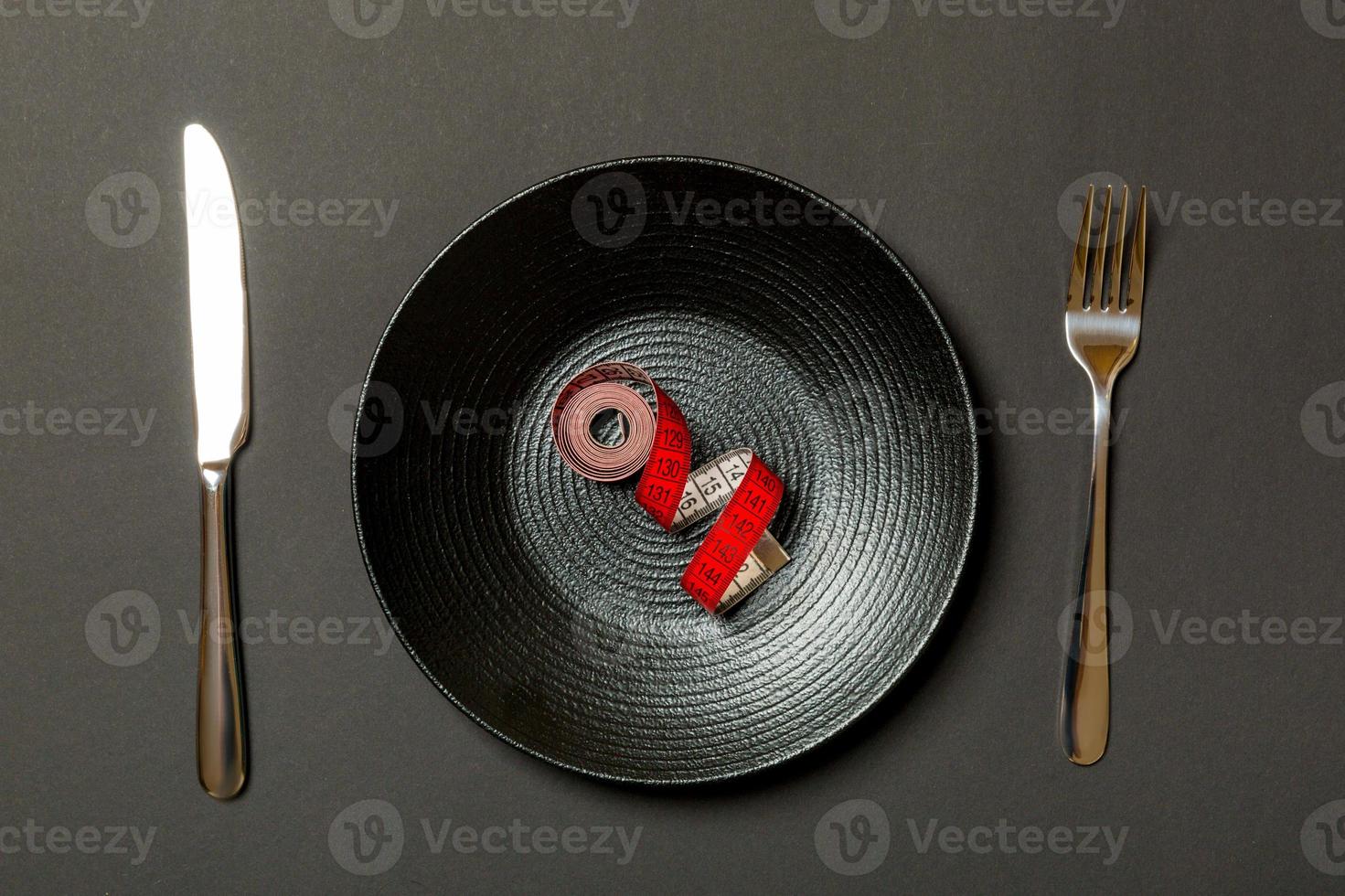 Healthy diet concept of plate with measuring tape, fork and knife on black background. Top view photo