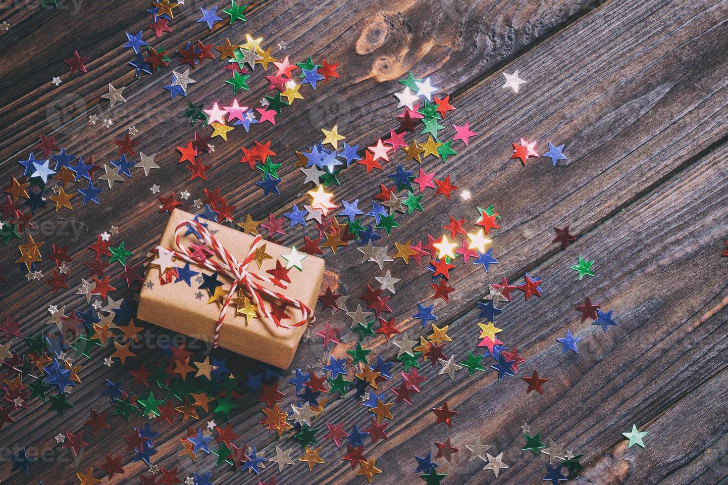 Gift box with star. Creative concept with festive decor on black background. Confetti stars, red, yellow with gift box. Explosion of confetti. Toned photo