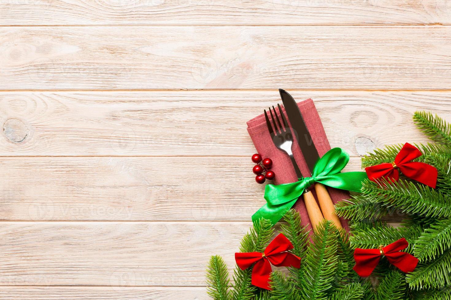 Top view of christmas decorations on wooden background. Fork and knife on napkin tied up with ribbon and empty space for your design. New year pattern concept photo