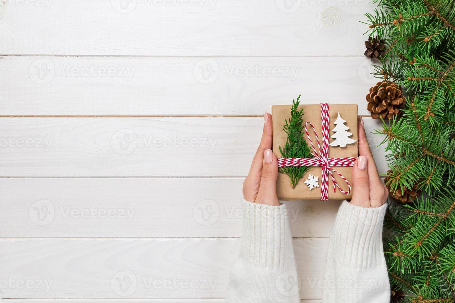 Woman hands give wrapped christmas handmade present in paper with christmas decoration. Present box on holiday on dark wooden table, top view photo