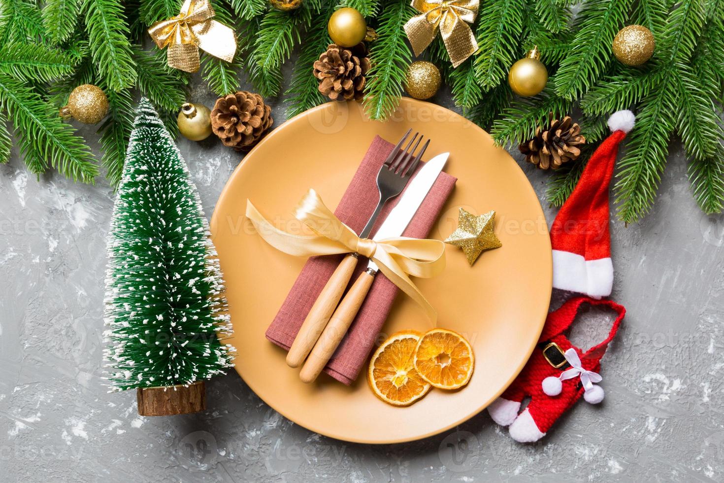 Top view of fork, knife and plate surrounded with fir tree and Christmas decoratoins on cement background. New Year Eve and holiday dinner concept photo