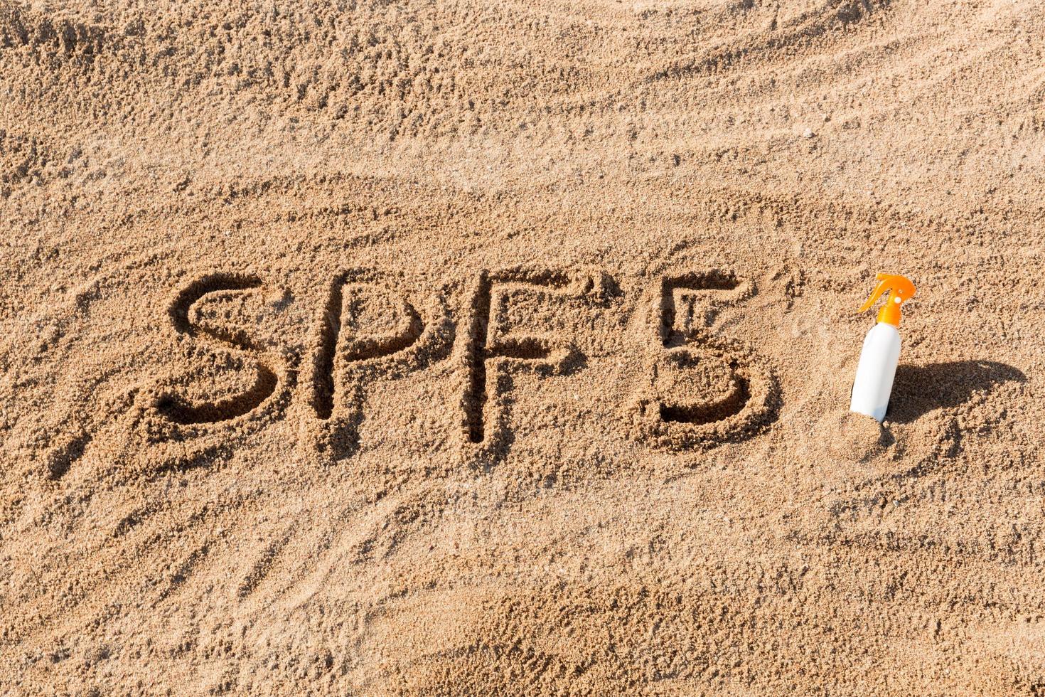 protección solar factor cinco. palabra spf 5 escrita en la arena y botella blanca con crema bronceadora. fondo del concepto de cuidado de la piel foto