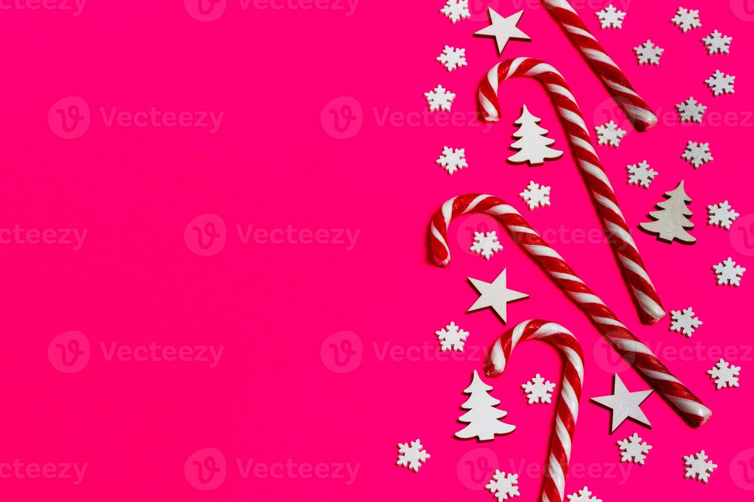 bastón de caramelo de navidad mintió uniformemente en fila sobre fondo rosa con copo de nieve decorativo y estrella. plano y vista superior foto
