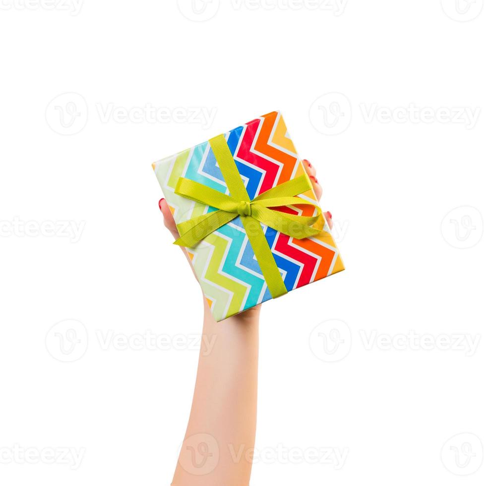 Woman hands give wrapped Christmas or other holiday handmade present in colored paper with green ribbon. Isolated on white background, top view. thanksgiving Gift box concept photo