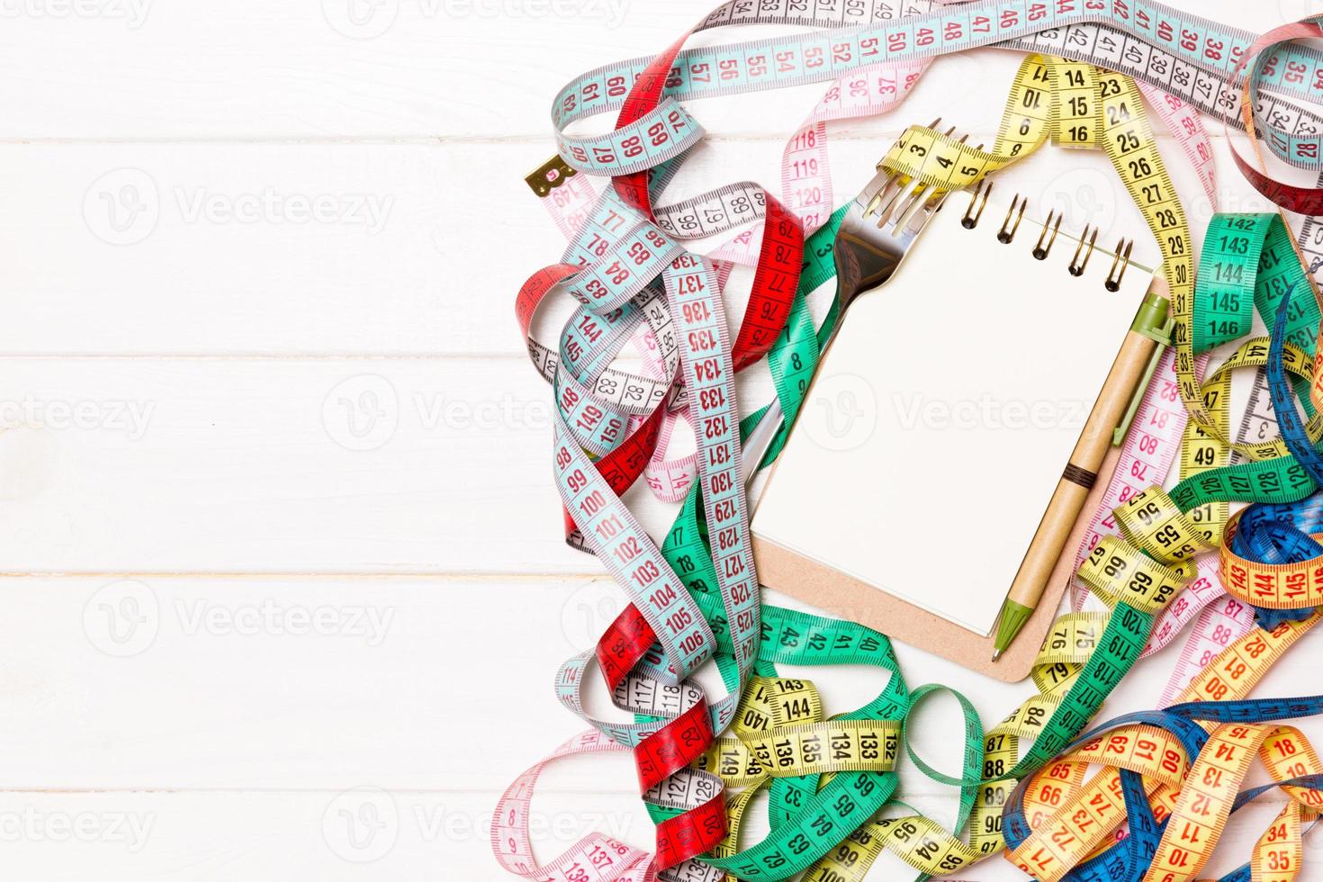 Group of colorful measure tapes, pen, open notebook and fork on wooden background with empty space for your idea. Top view of healthy lifestyle concept photo