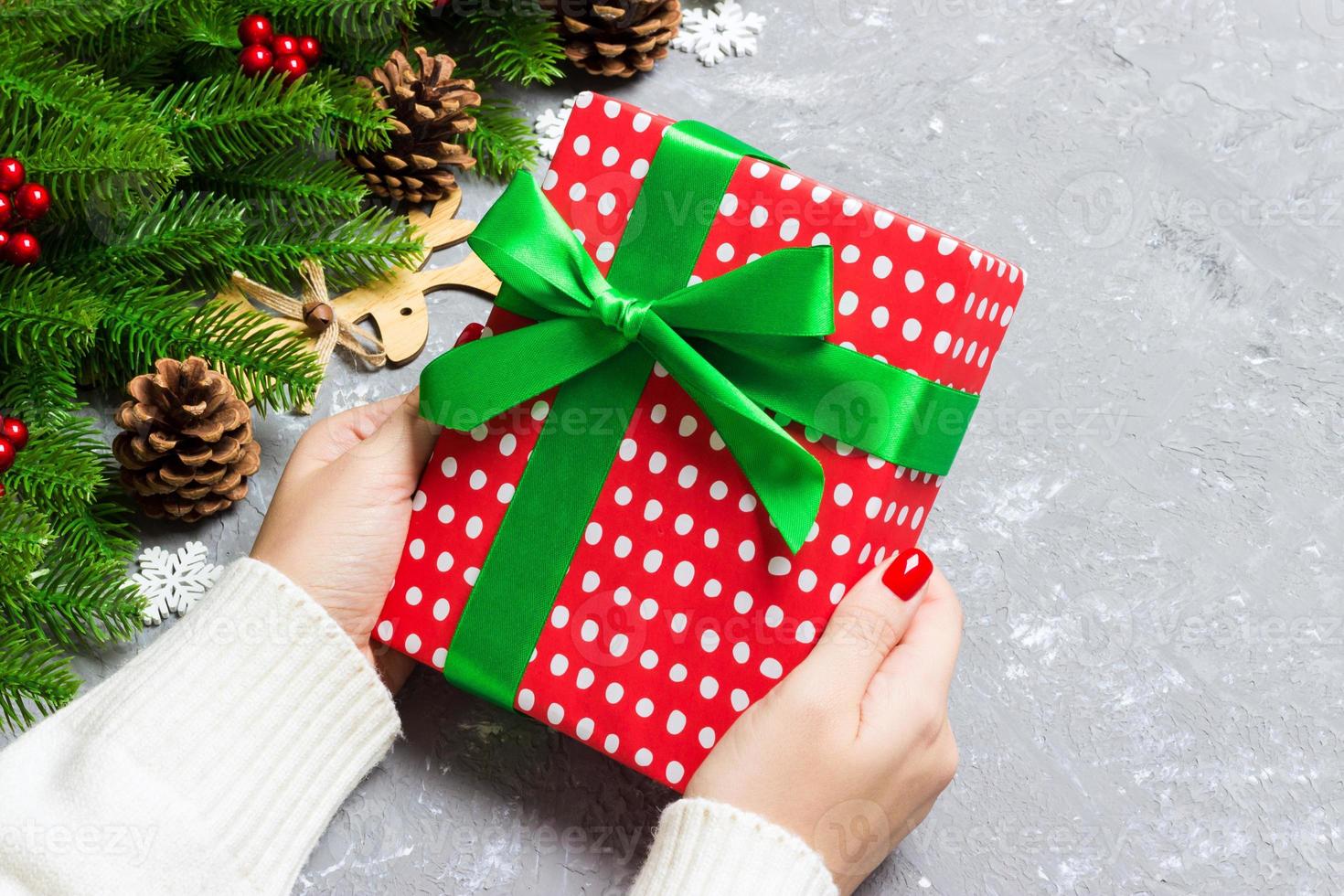 Top view of a woman holding a gift box in her hands on festive cement background. Fir tree and Christmas decorations. New year time concept photo