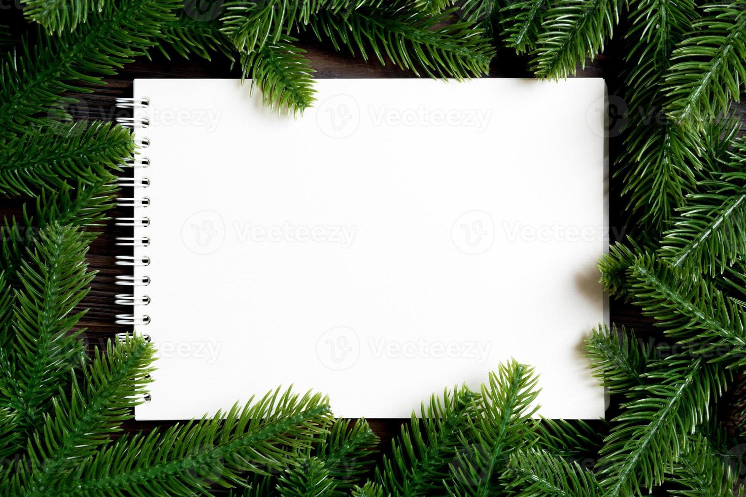 Top view of notebook decorated with a frame made of fir tree on wooden background. New Year time concept photo