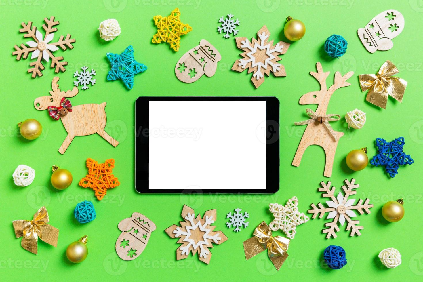 Top view of digital tablet on green background with New Year toys and decorations. Christmas time concept photo