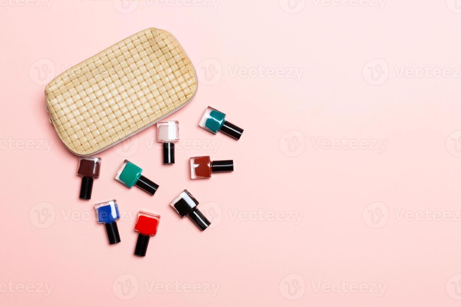 Top view of the set of nail polishes and bright gel varnishes fallen out of cosmetics bag with copy space on pink background. Trendy nail concept photo