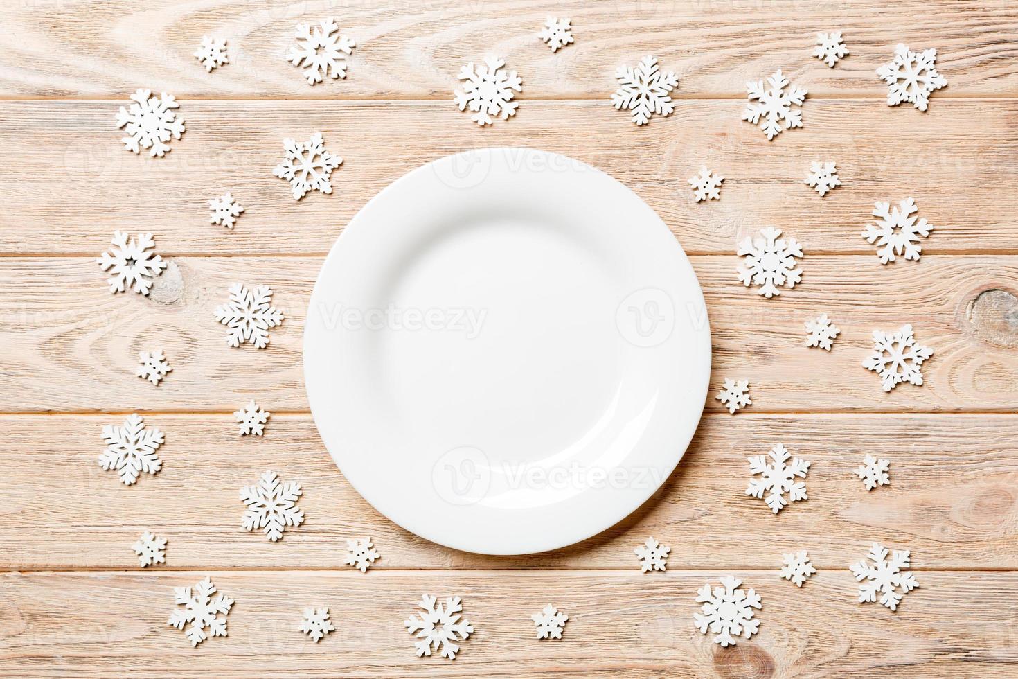 Top view of empty plate surrounded with snowflakes on wooden background. New Year dinner concept photo