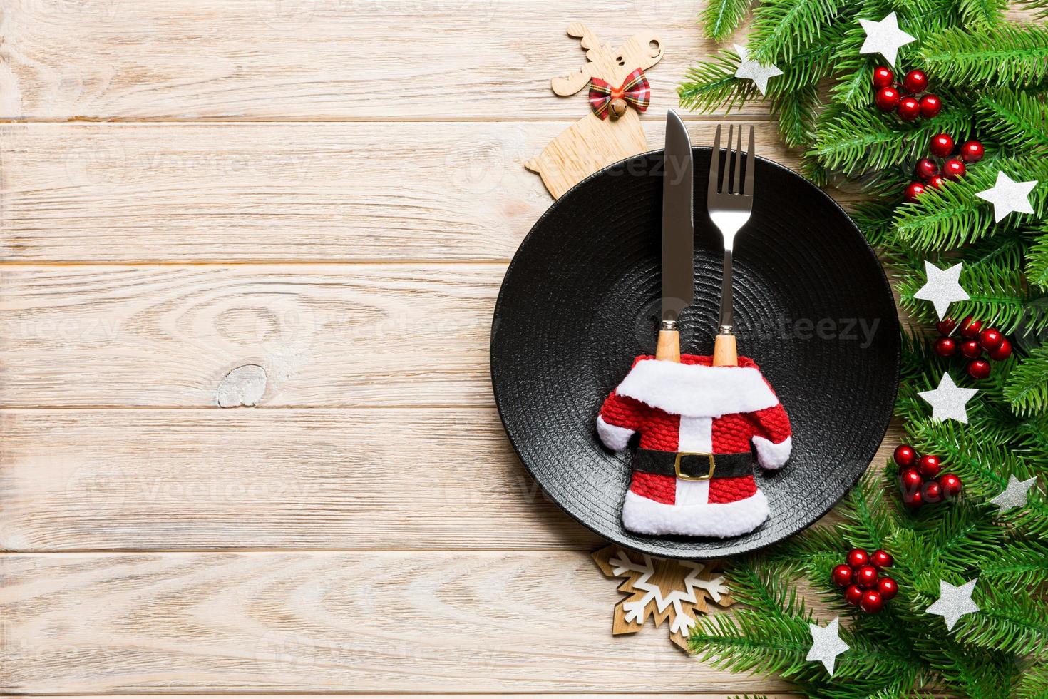 Top view of Christmas dinner on wooden background. Plate, utensil, fir tree and holiday decorations with copy space. New Year time concept photo