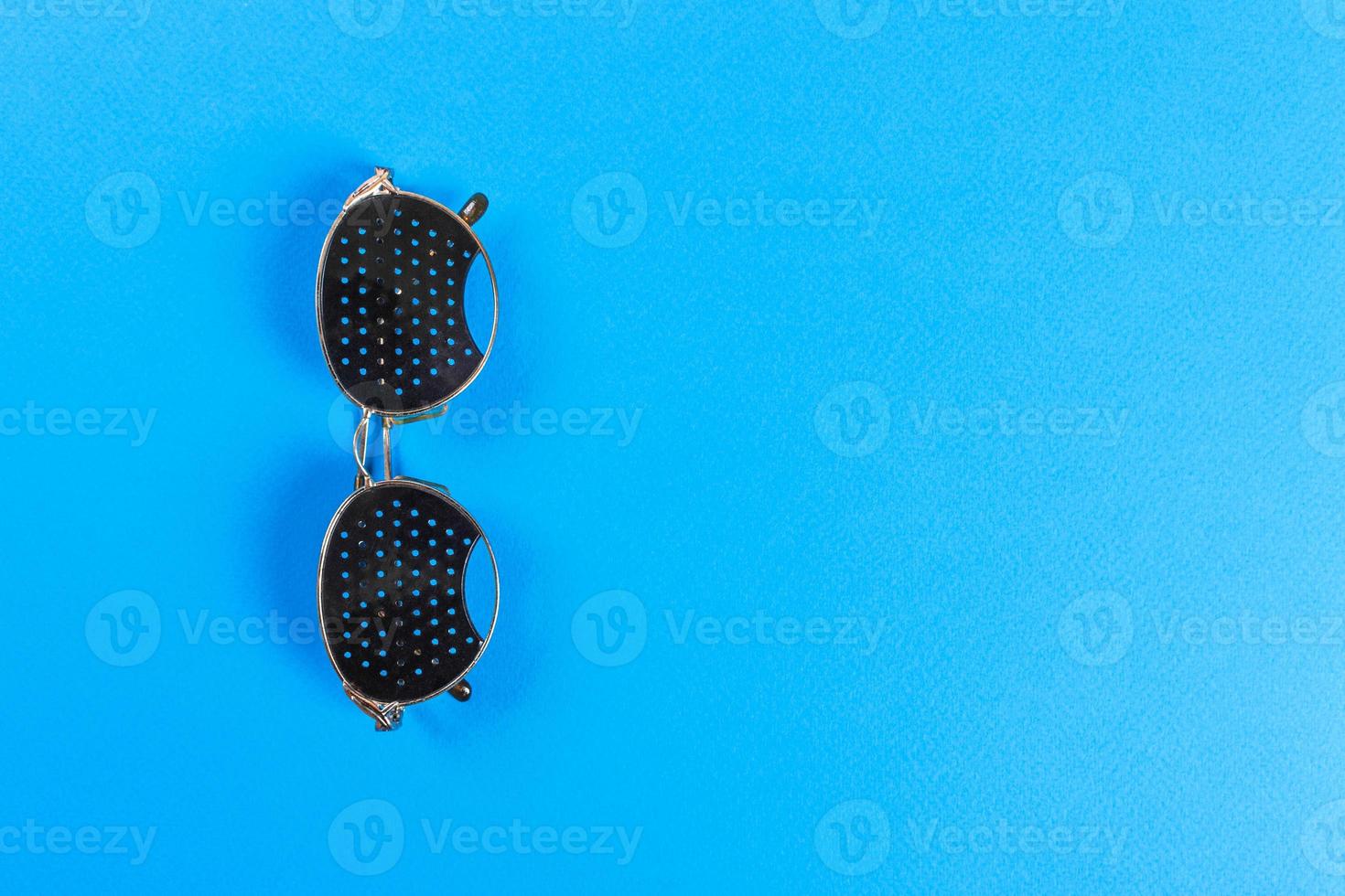Black pinhole glasses on blue background. Medical concept. Top view photo
