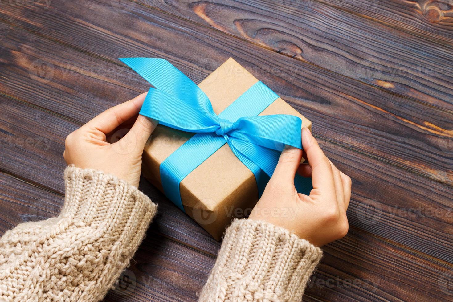 Girl tying a simple blue bow on a gift box. Wrapped in plain craft paper and Blue ribbon. Finishing touches photo