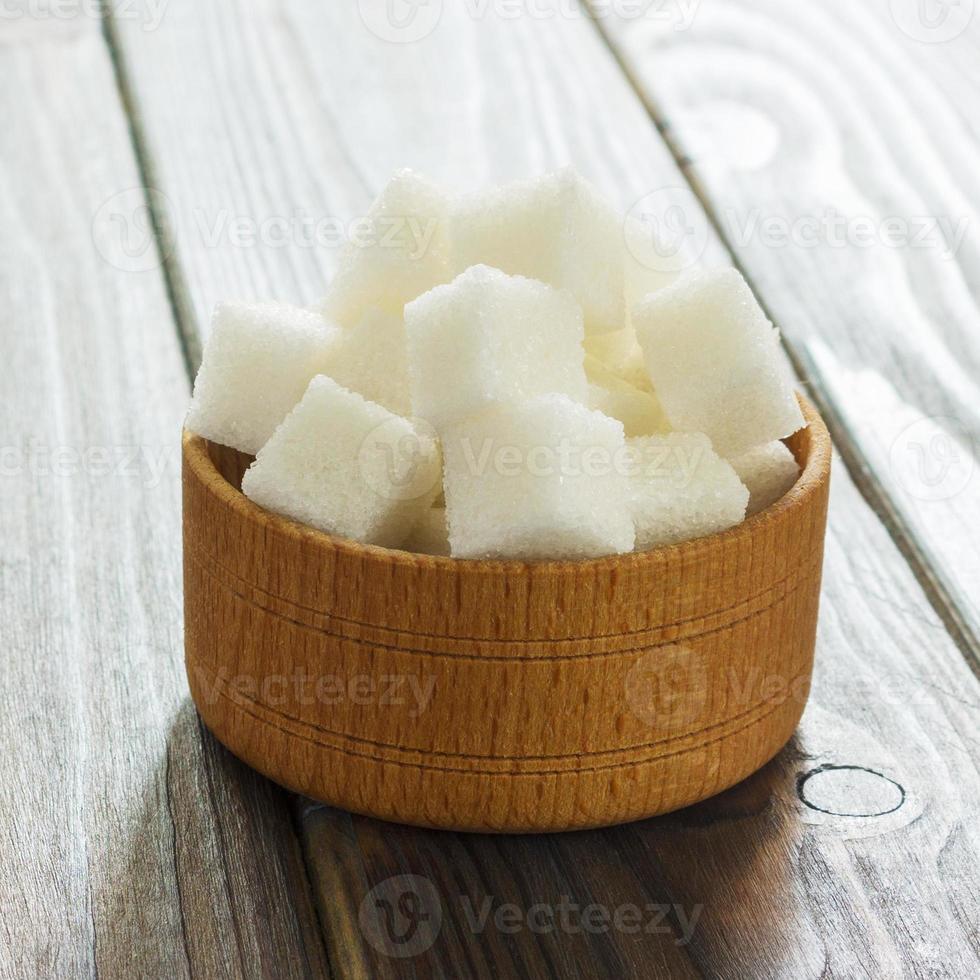 cubos de azúcar en un tazón sobre una mesa de madera. terrones de azúcar blanca en un tazón foto