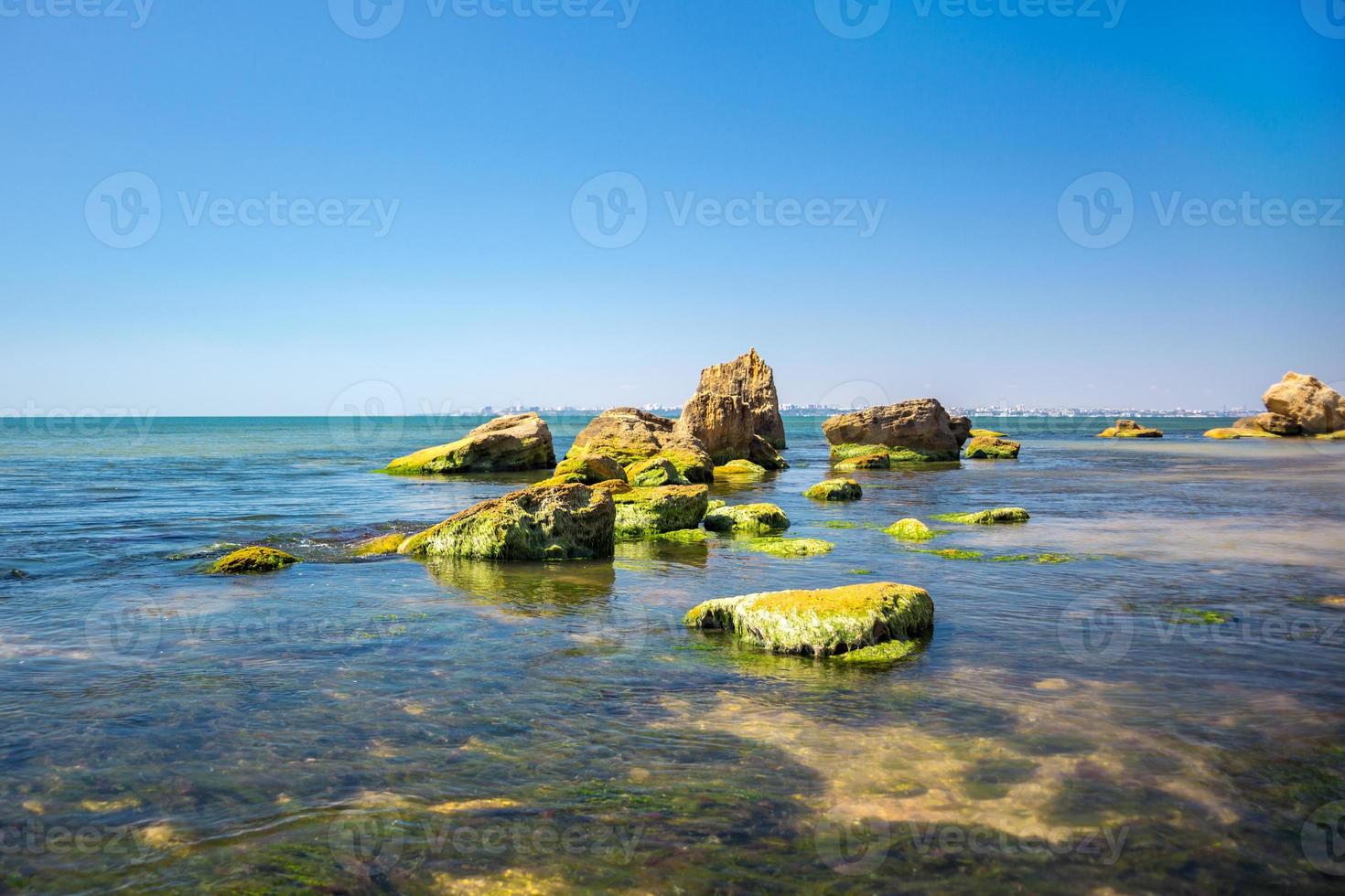 piedra cubierta de algas verdes en el mar con azul cielo como fondo. larga exposición. foto