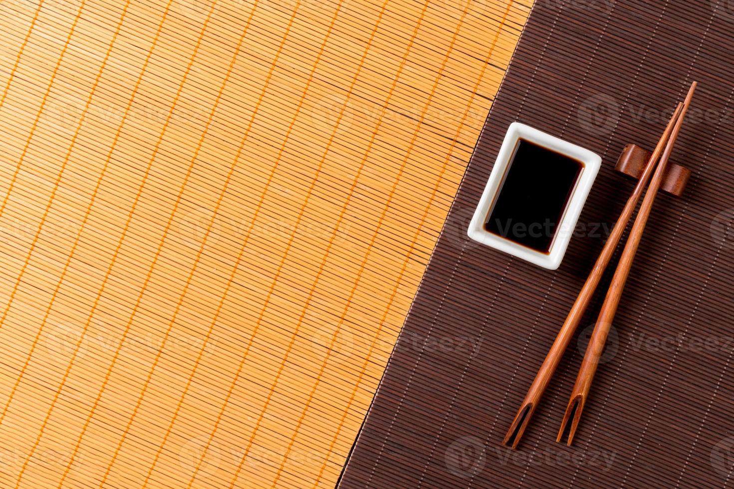 Chopsticks and bowl with soy sauce on two bamboo mat blak and yellow top view with copy space photo