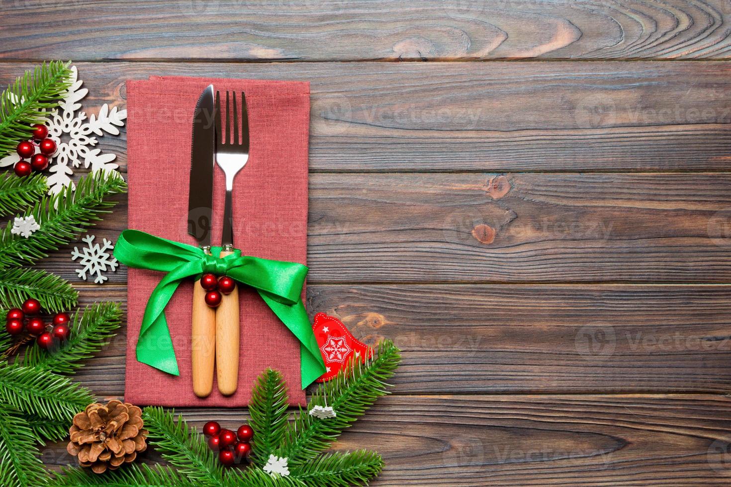 Top view of christmas decorations on wooden background. Fork and knife on napkin tied up with ribbon and empty space for your design. New year pattern concept photo