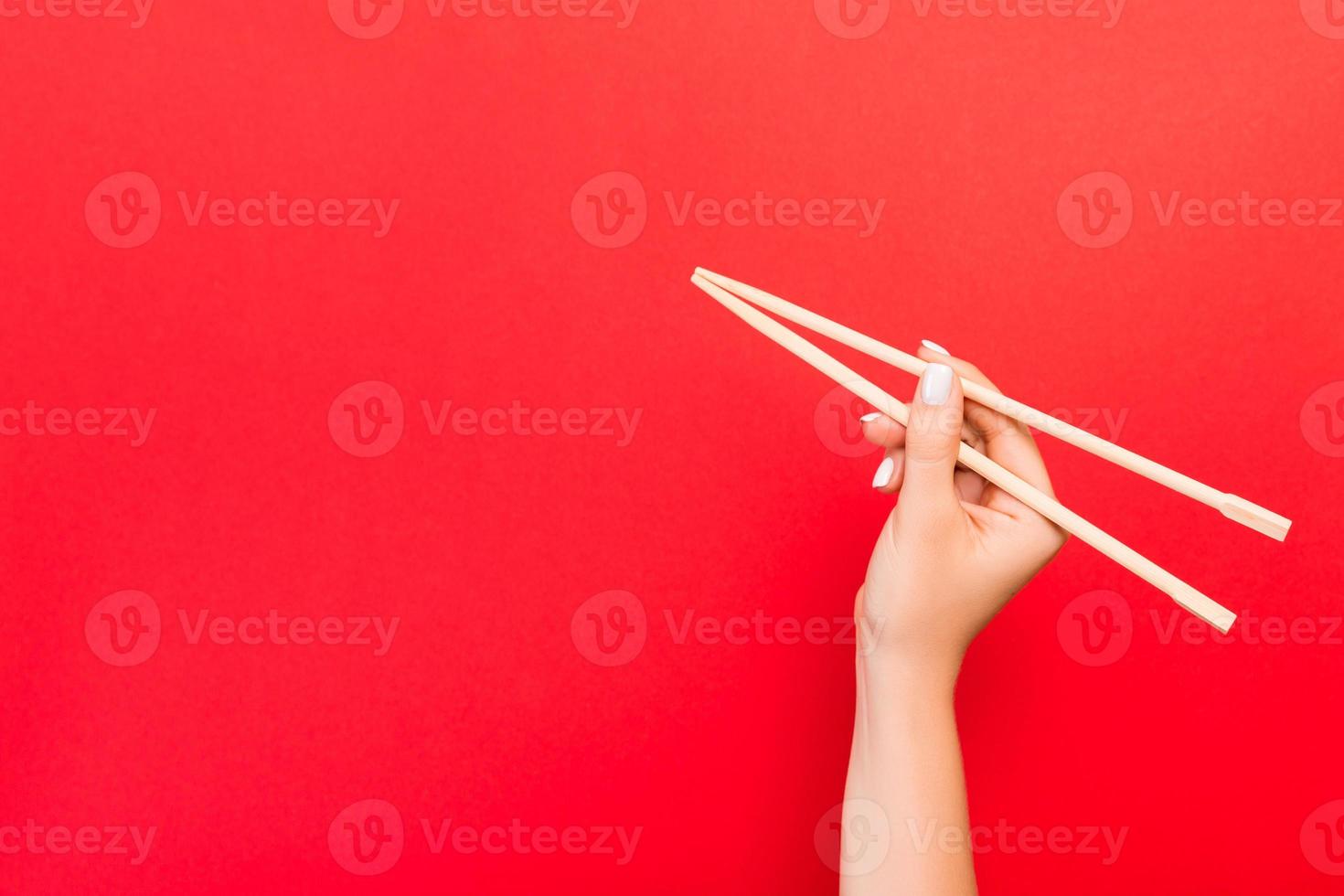 Woman's hand holding chopsticks on red background. Chinese food concept with empty space for your design photo