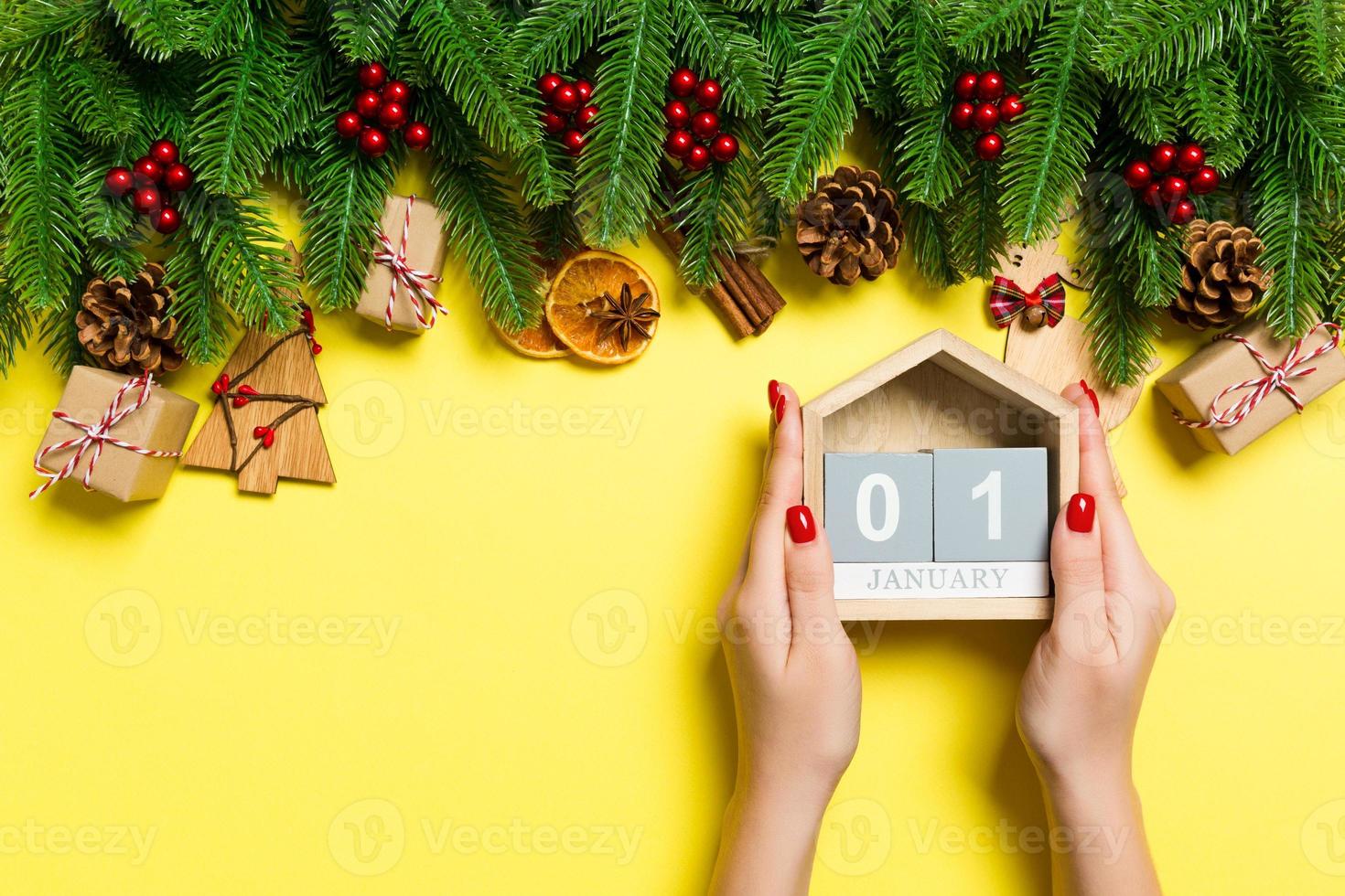 Top view of female hands holding calendar on yellow background. The first of January. Holiday decorations. New Year concept photo