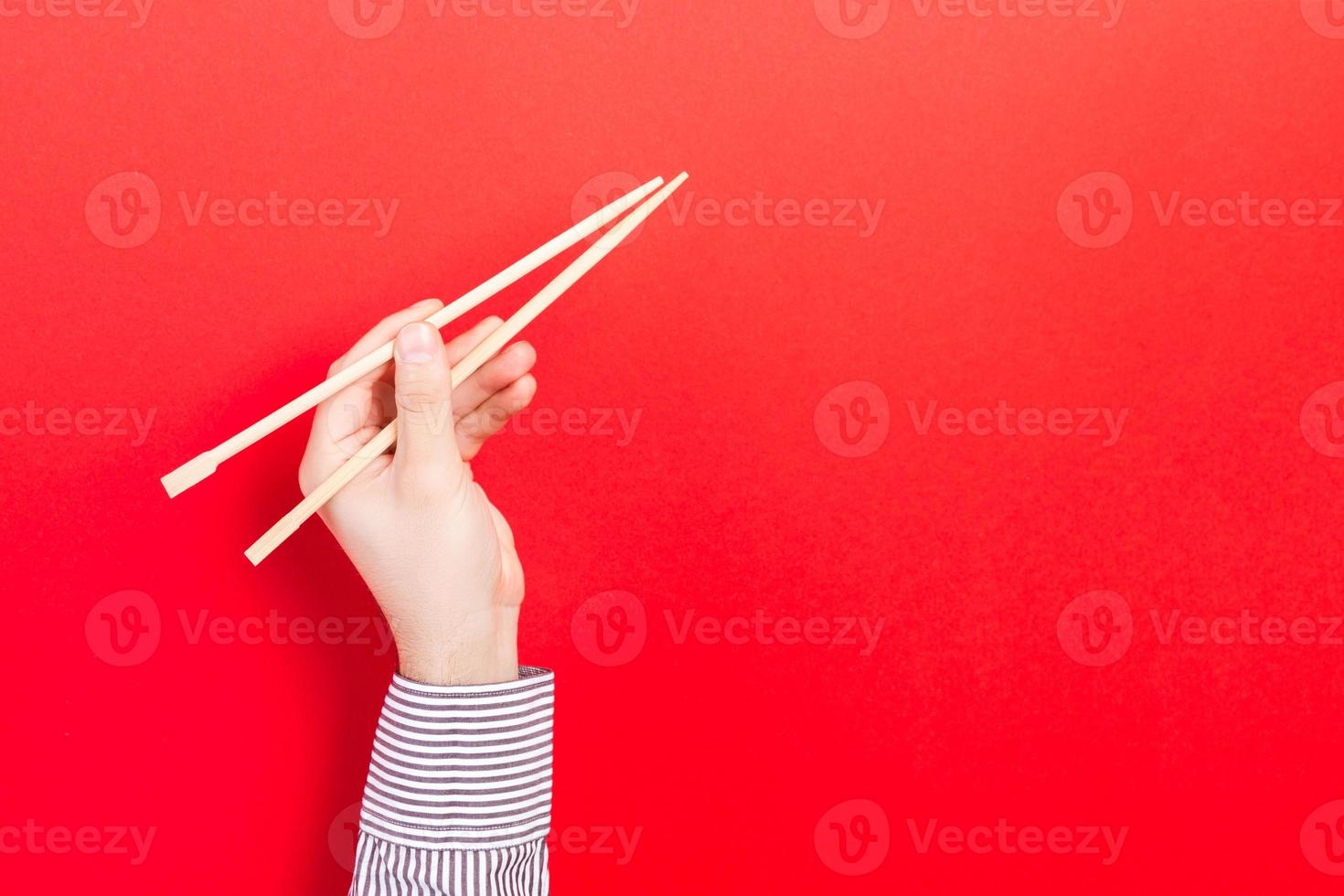 Wooden chopsticks in male hand on red background with empty space for your idea. Tasty food concept photo