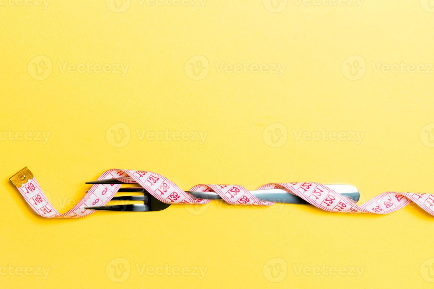 Composition of curled wrapped measuring tape and fork on yellow background. Overweight concept photo