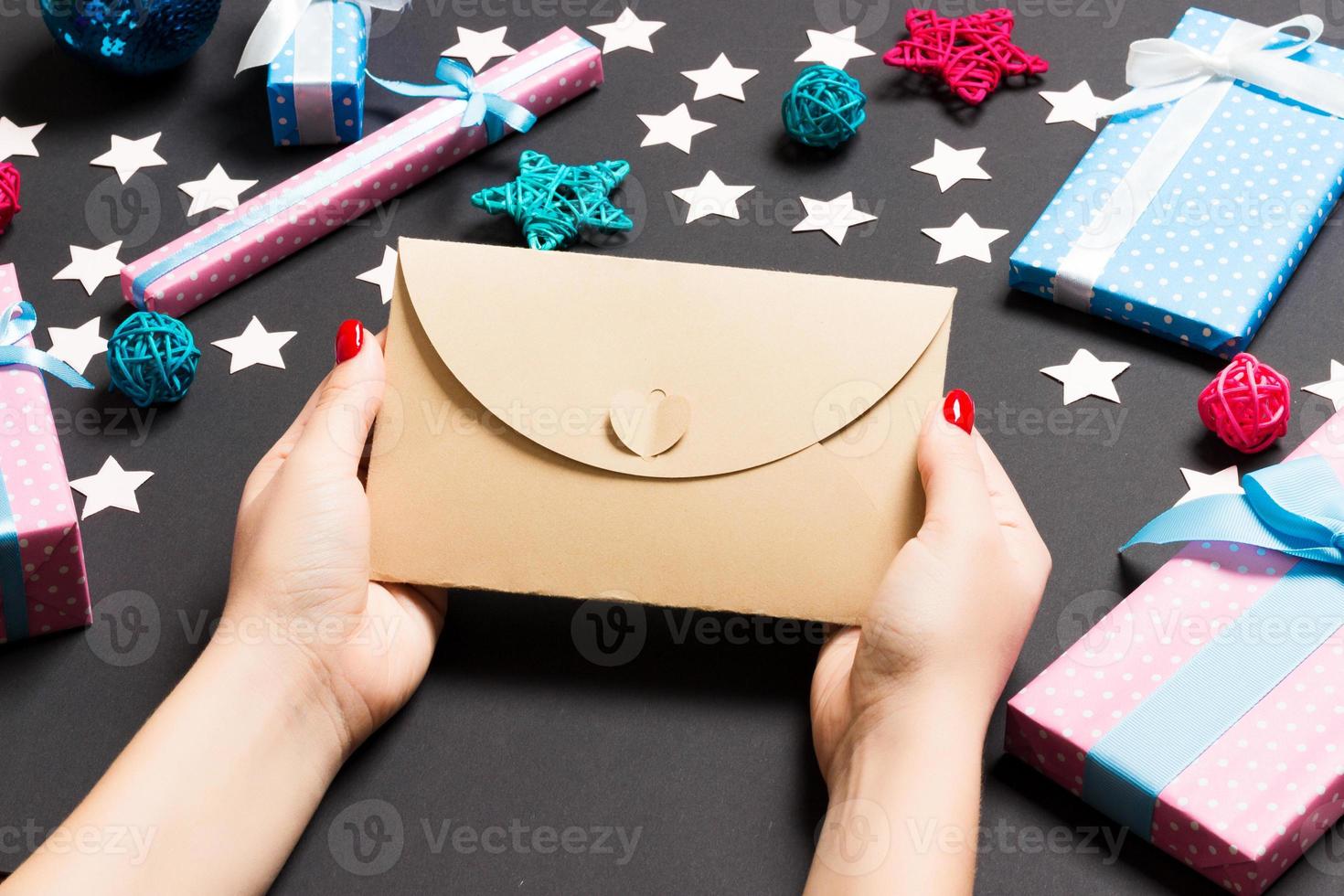 vista superior de una mujer sosteniendo un sobre sobre fondo negro hecho de decoraciones navideñas. concepto de tiempo de navidad foto