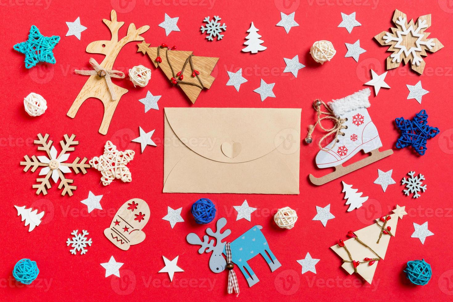 vista superior del sobre artesanal, juguetes navideños y decoraciones sobre fondo rojo de navidad. concepto de tiempo de año nuevo foto