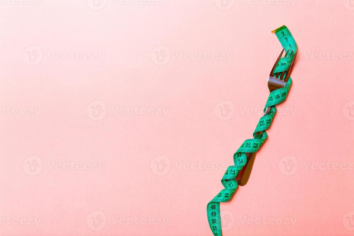 Fork wrapped in measuring tape on pink background with copy space. Top view of proper diet concept photo