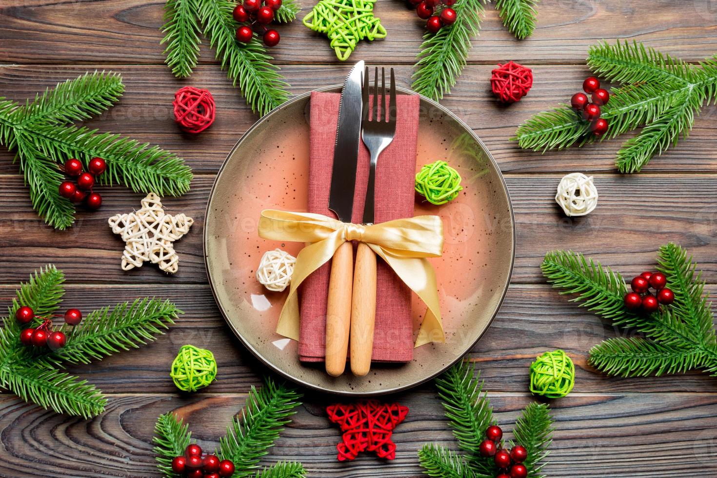 Holiday composition of plate and flatware decorated with Santa hat on wooden background. Top view of Christmas decorations. Festive time concept photo