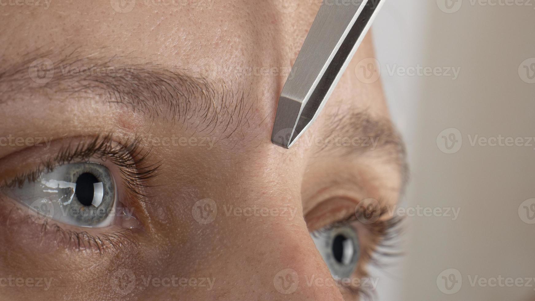woman plucking eyebrows with tweezers closeup photo