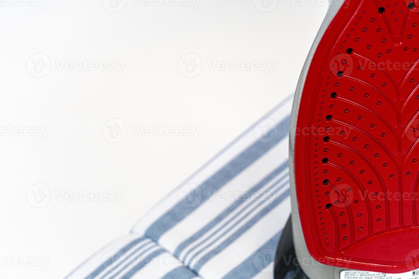 new clothes iron on white background, red ceramic iron, and blue fabric ironing board base photo