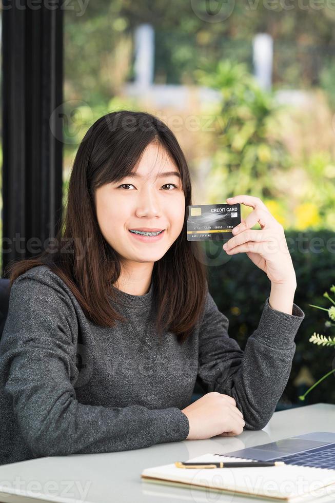 mujer joven sosteniendo una tarjeta de crédito con una computadora portátil en la cubierta foto