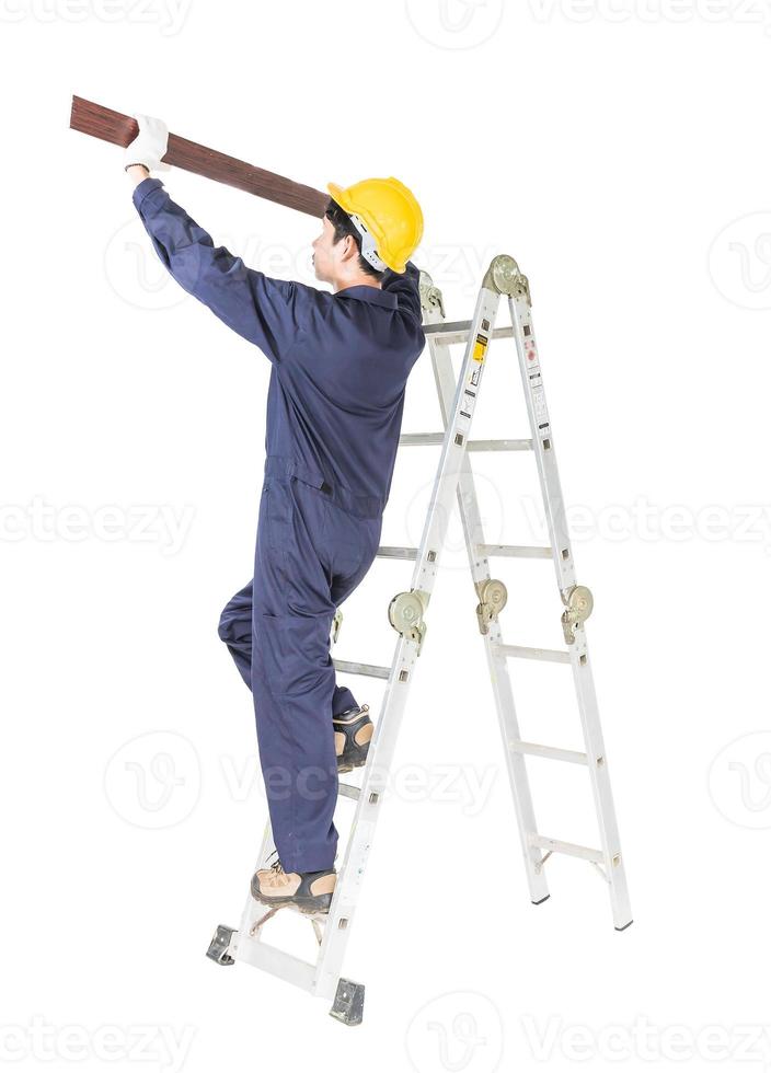 Handyman in uniform standing on ladder holding wood plank on white photo