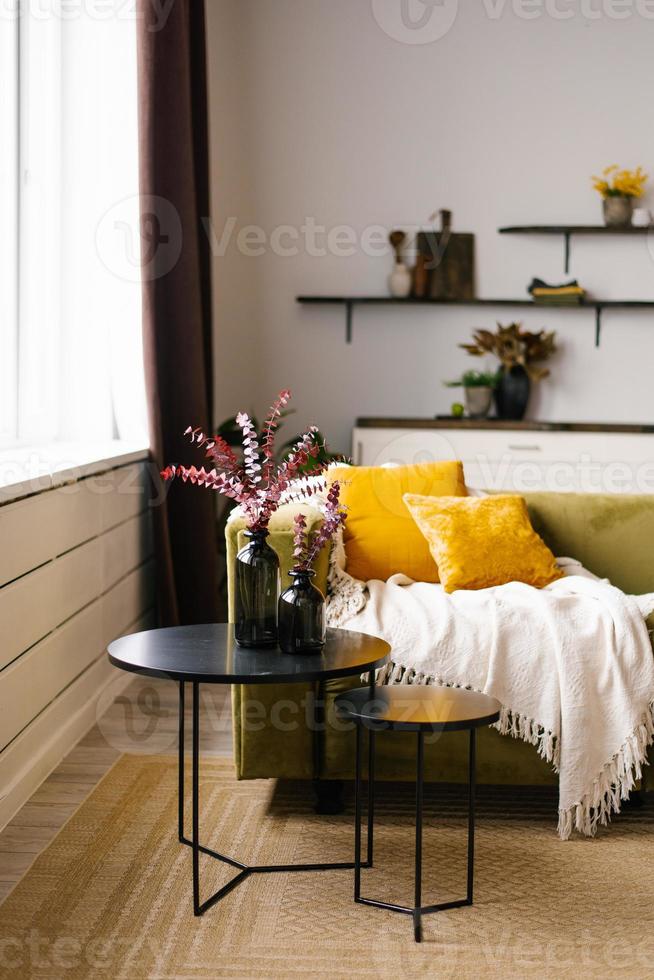 A green sofa with yellow pillows and a double black coffee table and a blanket in a modern Scandinavian-style living room interior photo