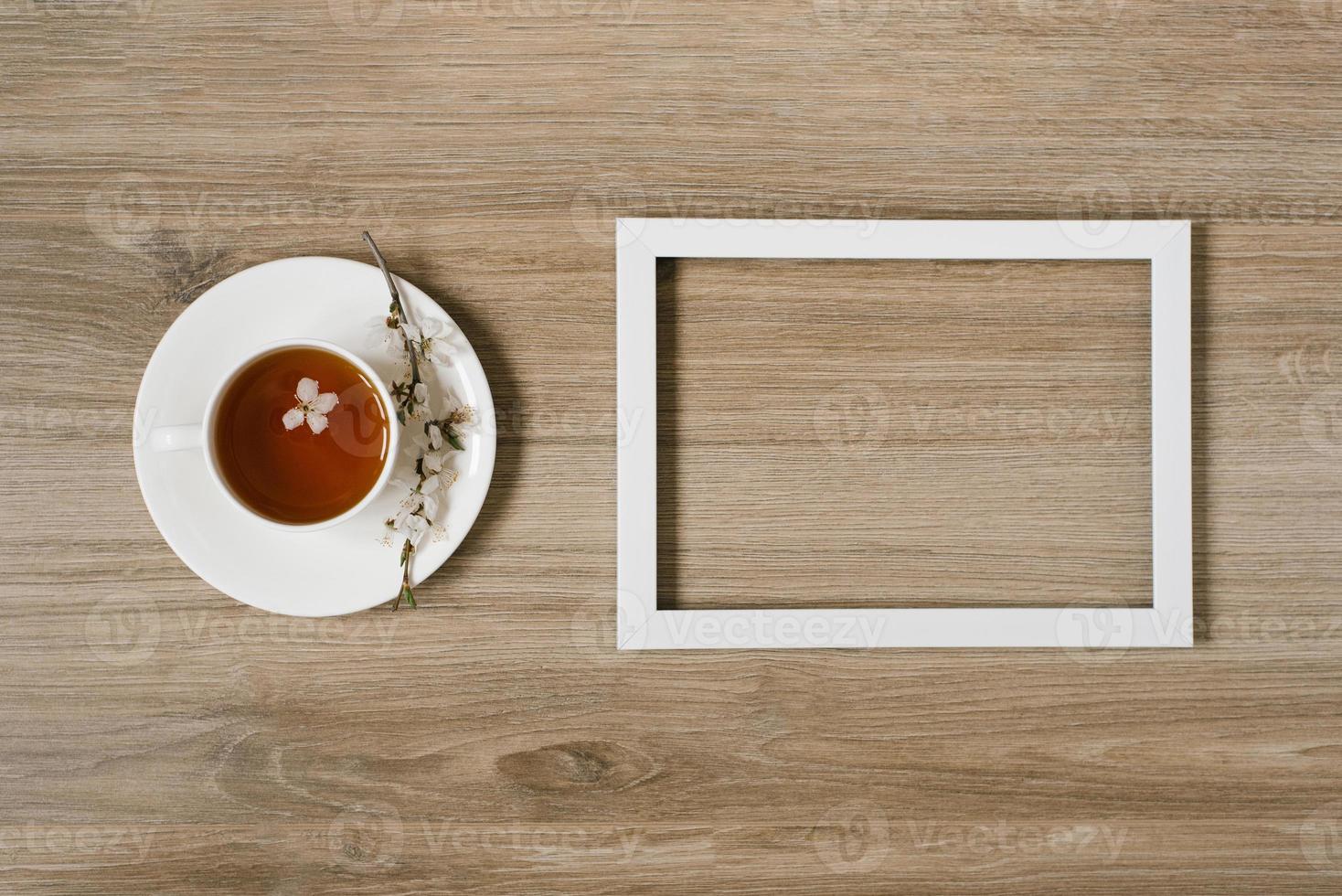 una taza blanca con té negro y una ramita de flor de manzana y un marco blanco sobre un fondo de madera. mocap y hasta prostranstva foto