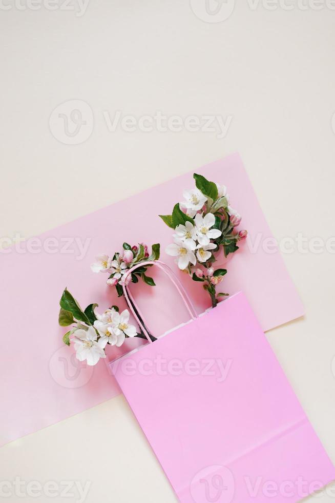 Branches of an apple tree with flowers lie in a paper shopping bag on a pink and beige background. Spring discounts and sales. Copy space photo