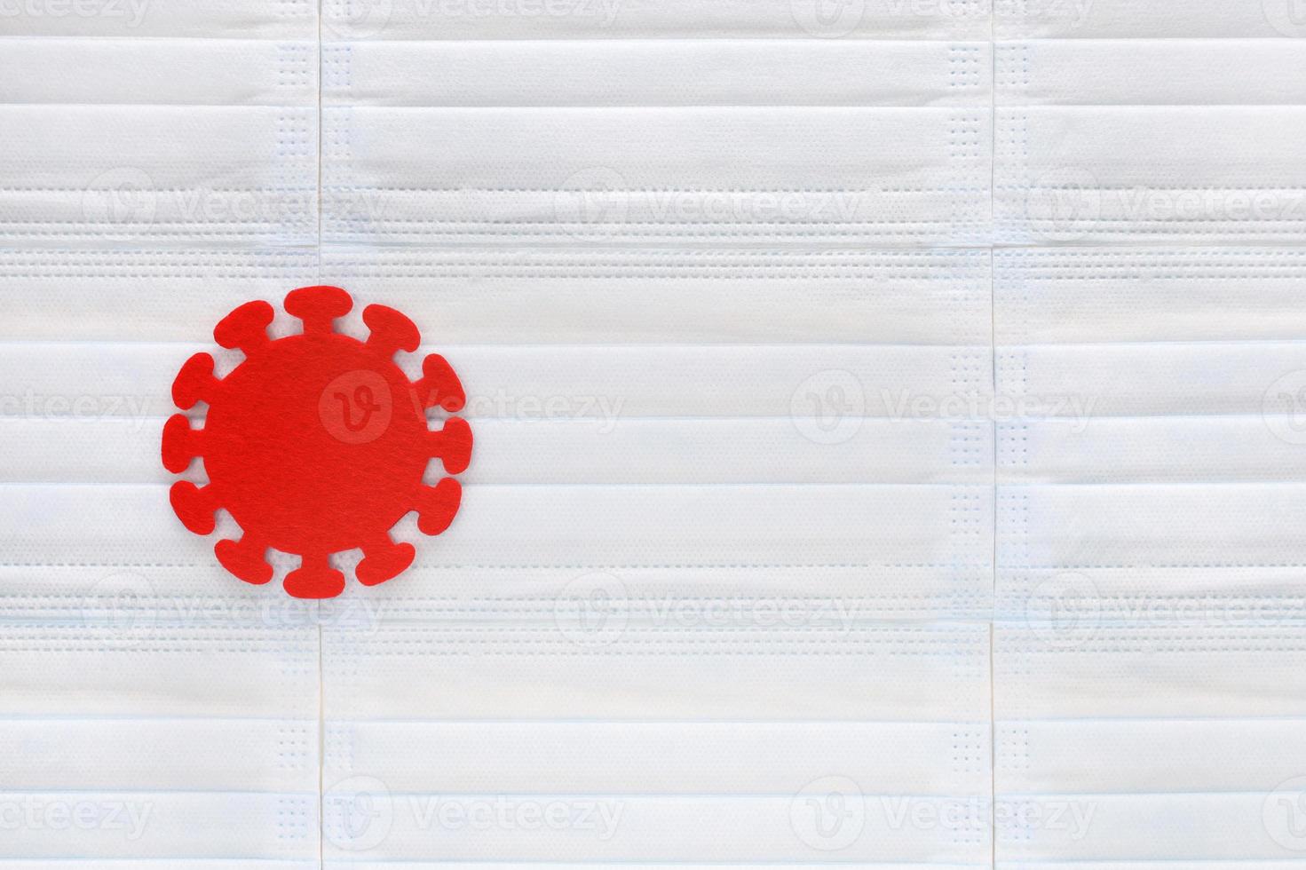 molécula de coronavirus cortada de fieltro rojo sobre fondo de máscaras médicas azul claro. pandemia mundial. estadísticas de enfermedades, vacunas, sistema de salud, medicina, cuarentena. concepto covid-19. foto