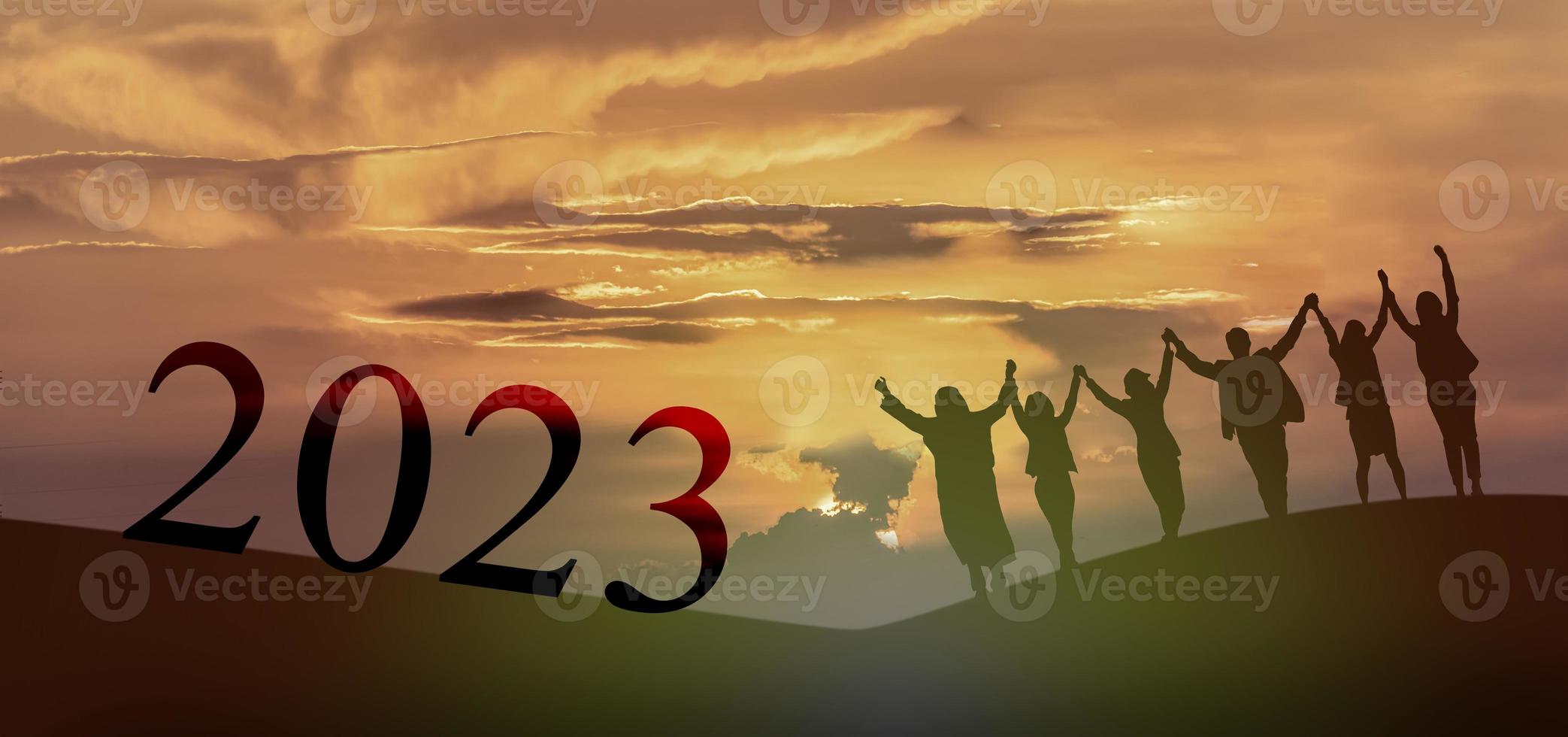 Happy new year 2023, Keep fighting together, Silhouette of 2023 letters on the mountain with business people raised arms in teamwork concept at sunrise. photo