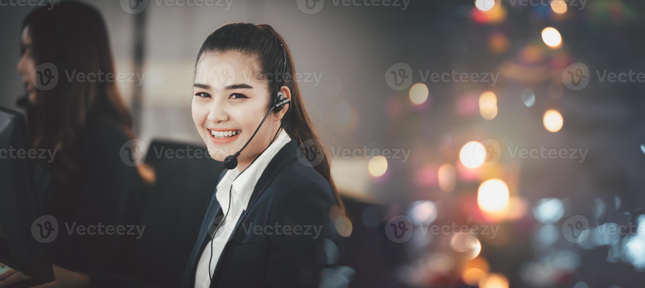 mujer asiática con auriculares, sentada en la oficina, trabajando como operadora del centro de llamadas o apoyando el servicio al cliente, mirando directamente a la cámara y sonriendo amigablemente. foto