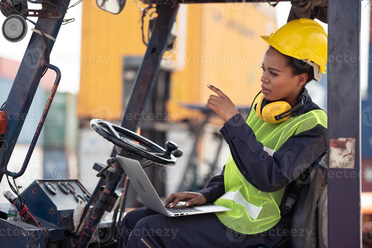 Female worker driving forklift and pointing hand in industrial container warehouse. photo