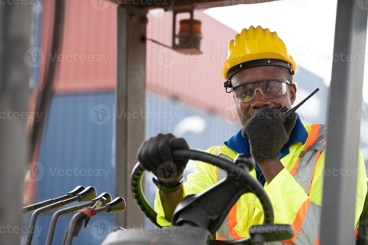 Worker man driving forklift in industrial container warehouse,talking on walkie talkie. photo
