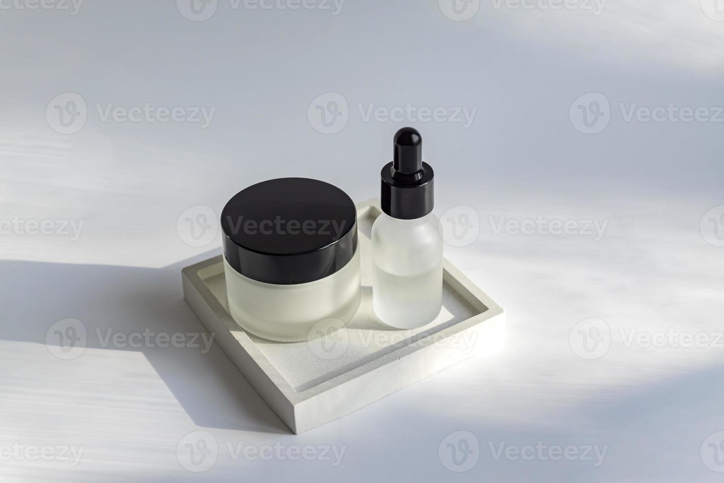 Set of skin and body care products in white matte glass blank packaging. Dropper bottle and cream jar. Unbranded package showcase. Mockup. photo