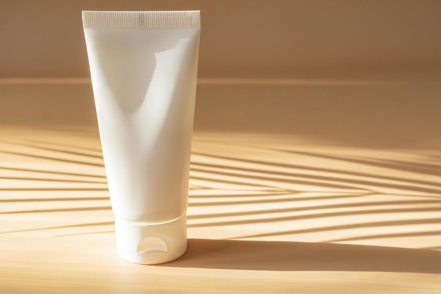 maqueta de tubo de plástico en blanco para cosméticos con tapa sobre fondo beige con sombras solares. diseño publicitario de moda de verano para cosméticos para el cuidado de la piel. foto