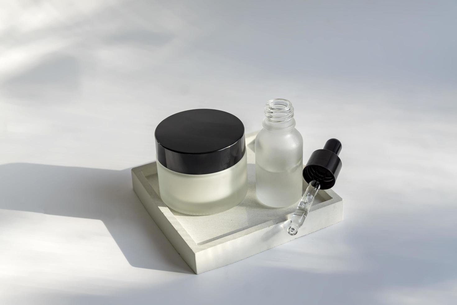 Set of premium cosmetics in matt glass jar and dropper bottle on concrete square plate. Skin care concept in minimalist style. Mockup. unbranded packaging. photo