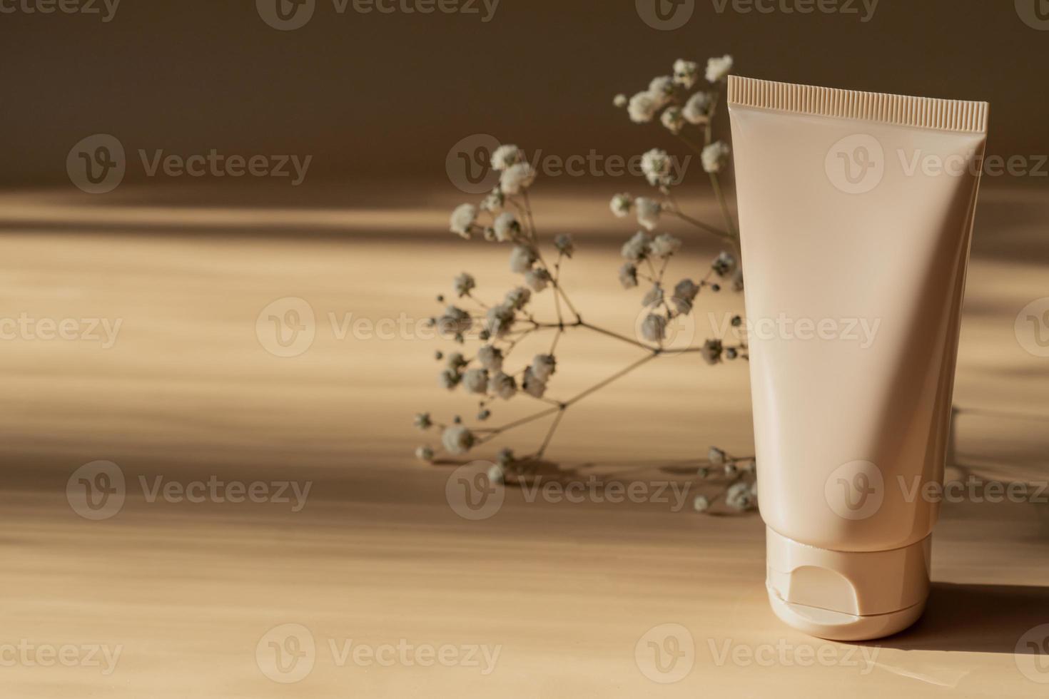 Unbranded white squeeze cosmetic cream bottle tube and dry gypsophila flower on beige background with harsh shadows. Natural oranic spa cosmetics concept. Mockup, template, front view photo