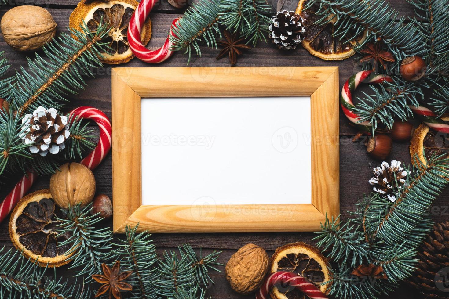 Frame of Christmas tree cones oranges caramel cane nuts on dark wooden background. Copy space. Flat lay. Wooden frame and space for text. photo