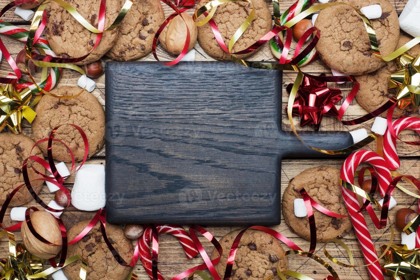 galletas con trocitos de chocolate bastones de navidad caramelo oro rojo paisaje y malvavisco sobre fondo de madera. copie el marco del espacio. foto