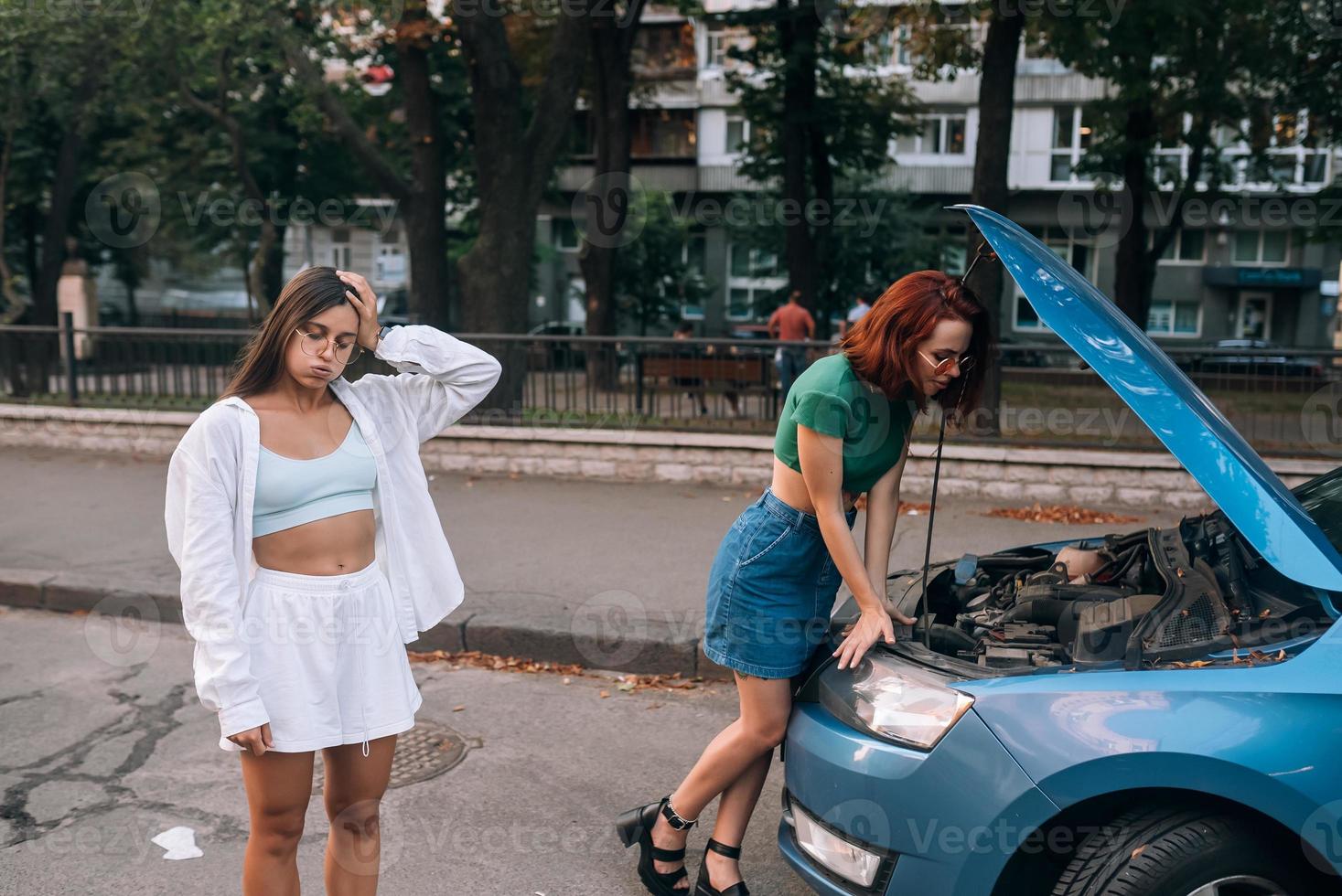 Two women with broken car on the road. Open hood photo