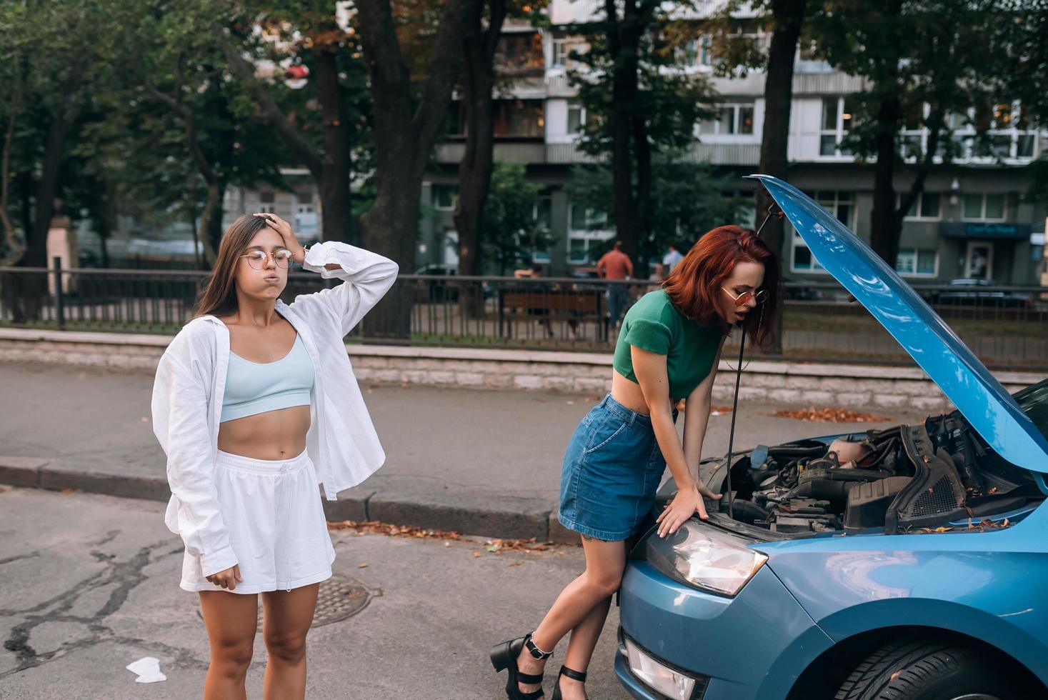 Two women with broken car on the road. Open hood photo