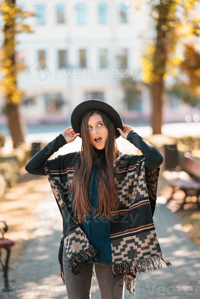 Stylish woman in poncho and hat enjoys autumn's park photo